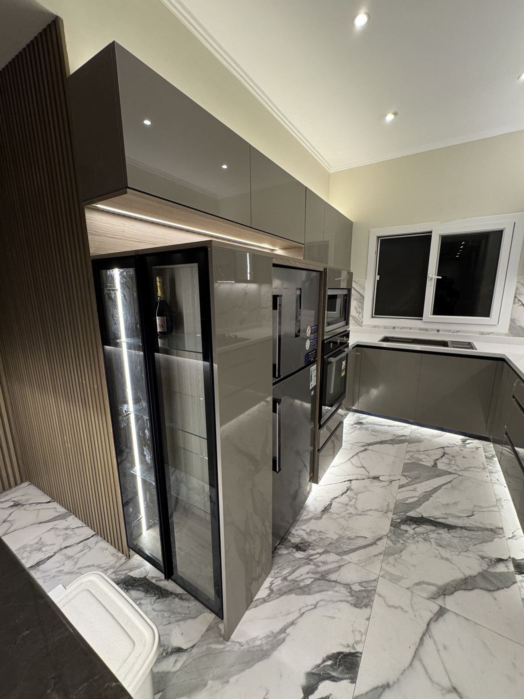Taupe gloss kitchen with tall appliance units and LED plinth light